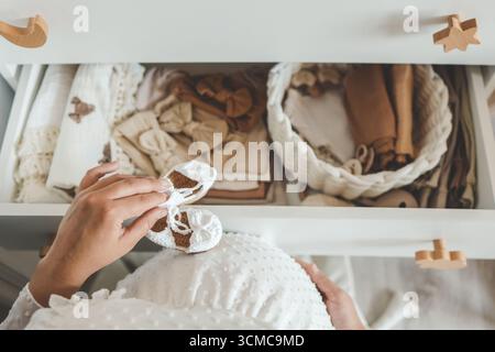Handgefertigte Strickschuhe für Kinder in den Händen. Schwangere Frau bereitet sich auf die Entbindungsklinik vor und packt Babysachen. Präparat der schwangeren Frau Stockfoto