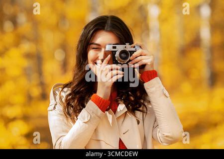 Porträt von glücklichen weiblichen Fotografen mit Retro-Kamera fotografieren Von schönen Herbst im Park Stockfoto