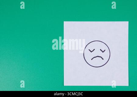 Trauriges Emoji-Symbol auf einer Post-it-Notiz mit grünem Hintergrund und Kopierraum Stockfoto
