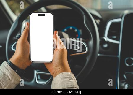Ein Telefon mit einem isolierten Bildschirm in den Händen einer Frau in einem Auto. Stockfoto