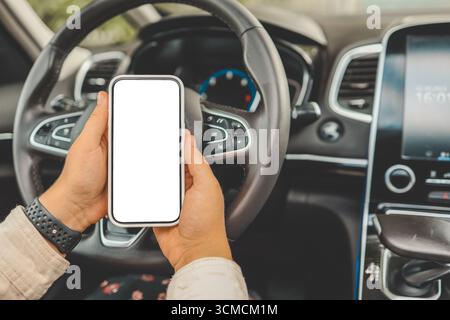 Ein Telefon mit einem isolierten Bildschirm in den Händen einer Frau in einem Auto. Stockfoto