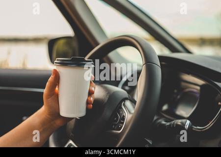 Pappbecher mit Kaffee in der Hand, Fahrt mit dem Auto. Stockfoto