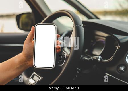 Ein Telefon mit einem isolierten Bildschirm in den Händen einer Frau in einem Auto. Stockfoto
