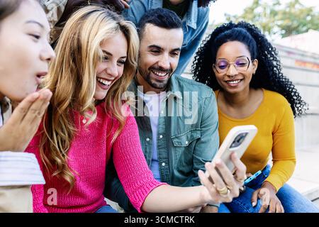 Glückliche multirassische Millennial-Freunde, die sich im Freien mit Mobiltelefonen amüsieren Stockfoto
