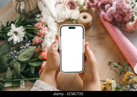Telefon in den Händen mit isoliertem Bildschirm auf einem Hintergrund aus Blumen. Stockfoto