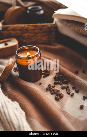 Eine brennende Kerze mit dem Geruch von Kaffee, ein offenes Buch und ein Stapel gemütlicher Pullover, ein ästhetisches Bild. Stockfoto