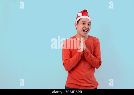 Fröhliche junge Person mit weihnachtsmütze in festlicher roter Kleidung, die weihnachten auf blauem Hintergrund feiert Stockfoto