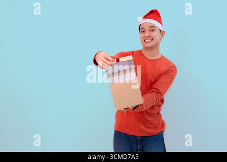 Glücklicher junger Mann in festlichem Outfit, mit Weihnachtsmütze und einer offenen Geschenkbox für weihnachtskonzept vor blauem Hintergrund Stockfoto
