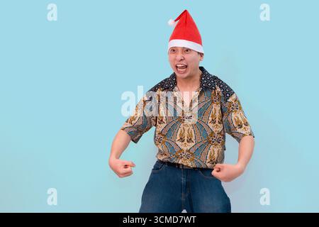 Junger Mann trägt Batik und weihnachtsmann-Hut drücken fröhlich und fröhlich auf blauem Hintergrund aus Stockfoto