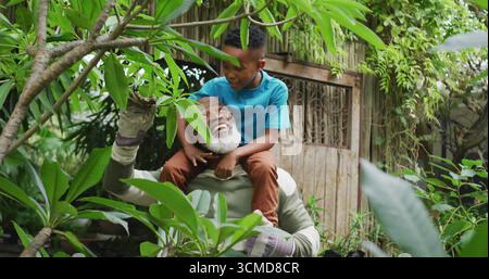 Großvater trägt Enkel auf Schultern und beschneidet Zweige im Garten, mit Gartenhandschuhen Stockfoto