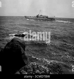 Dieses stimmungsvolle Archivfoto aus den 1970er Jahren zeigt eine berühmte Szene eines sowjetischen Urlaubs auf der Krim. Ein typisches Passagierausflugsboot des Projekts 1430, der Typ „Alexander Grin“, segelt auf den Wellen des Schwarzen Meeres entlang der Küste. Diese Schiffe waren das wichtigste Transportmittel für beliebte Seeausflüge zwischen Kurorten. Das Bild, das von einem felsigen Ufer aufgenommen wurde, vermittelt perfekt den Geist der Reise und des Abenteuers, der während der „Ära der Stagnation“ ein integraler Bestandteil eines Urlaubs im Hauptort der UdSSR war. Stockfoto