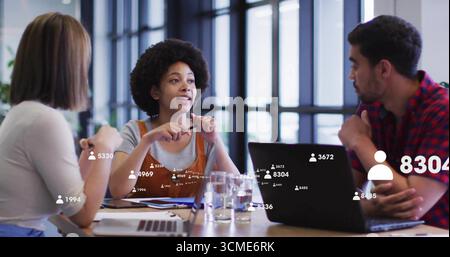 Eine lebhafte, lockhaarige Frau, die im Besprechungsraum diskutiert, mit Laptops und Papieren Stockfoto