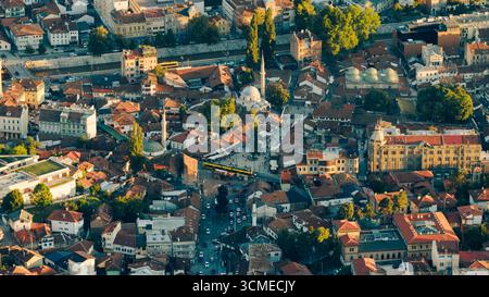 Drohnenblick auf den Bascarsija-Platz in der Altstadt von Sarajevo mit Moscheen, historischen Gebäuden und umliegenden Straßen im Abendlicht Stockfoto
