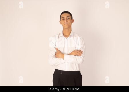 Ein junger Mann, der mit gekreuzten Armen steht und selbstbewusst in die Kamera blickt Stockfoto