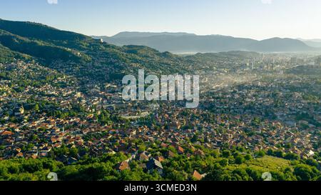 DefaultWide Panoramablick von Drohnen auf Sarajevo mit Wohnhäusern, Hügeln und Morgenlicht, die das Tal erleuchten Stockfoto