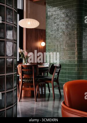 Café-Inneneinrichtung: Holztisch und Stühle in der Nähe von grün gefliesten Wänden und Glasfenster. Leerer Speisesaal im modernen Stil der Mitte des Jahrhunderts. Stockfoto