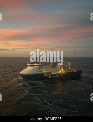 Das Schiff Norside Cygnus im Nordsee-Windpark bei Sonnenuntergang unterstützt die Wartung von Offshore-Turbinen und Projekte zur Förderung erneuerbarer Energien. Stockfoto