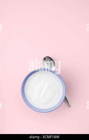 Frischer natürlicher Joghurt in blauer Schüssel auf rosa sauberem Hintergrund Stockfoto