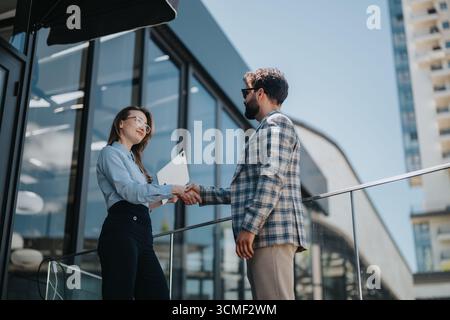 Geschäftlicher Handschlag zwischen ukrainischer Geschäftsfrau und türkischem Geschäftsmann im Freien in der Nähe eines modernen Bürogebäudes Stockfoto
