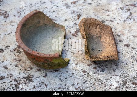 Eine kaputte und schmutzige alte Tonschale liegt zerbrochen auf einem Betonboden Stockfoto