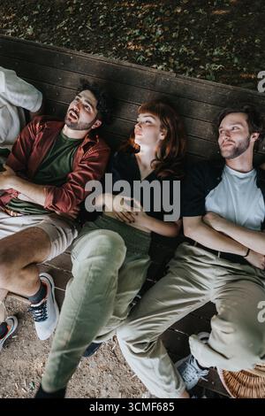 Drei Freunde ruhen sich auf einer Holzbank in einer ruhigen Umgebung im Freien aus Stockfoto
