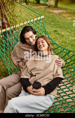 Zwei Liebhaber entspannen sich in einer Hängematte und teilen sich Lachen und Wärme in einem sonnendurchfluteten Park. Stockfoto