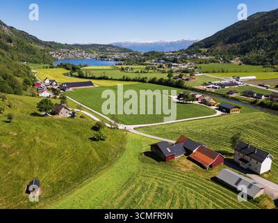 Atemberaubende Drohnenansicht auf ein malerisches norwegisches Dorf in einem grünen Tal mit einem Fjord und schneebedeckten Bergen. Stockfoto
