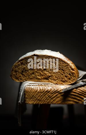 Hausgemachtes Roggensauerteigbrot in Abschnitt mit Messer auf einem rustikalen Holzhocker. Lebensmittelfotografie Stockfoto