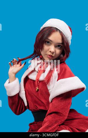 Junge Frau, die weihnachtskostüm trägt und mit ihren Haaren auf blauem Hintergrund spielt Stockfoto
