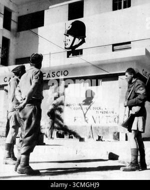 In Einem Bengasi-Platz – britische Tommien tauschen Geschichten auf einem Platz in Bengasi aus, nachdem die Deutschen aus der Stadt vertrieben worden waren. Mussolinis Porträt ist auf die Wand eines lokalen Kinos gerichtet. Ein „V für Sieg“ wurde über ein anderes italienisches Zeichen verschmiert. Dezember 1942. (Foto von AP Wirephoto). Stockfoto