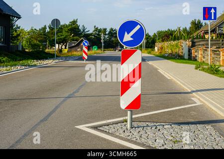 Verkehrsbremse mit rot-weiß gestreiften Barrieren und blauen Richtungspfeilen auf einer asphaltierten Straße, Sicherheitsmaßnahme im städtischen Straßenverkehr Stockfoto