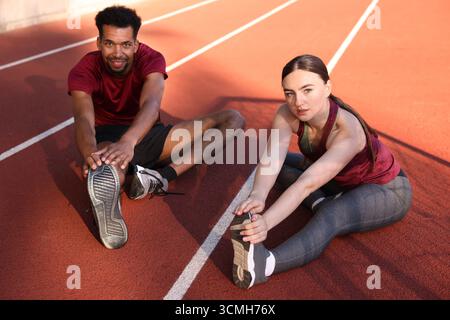 Ein Paar in Sportbekleidung, das sich vor dem Laufen im Stadion dehnt Stockfoto