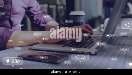 Asiatischer Mann, der lila Hemd trägt, tippt auf Laptop im Café, mit Smartphone-Kaffeetasse, schwimmenden Symbolen Stockfoto