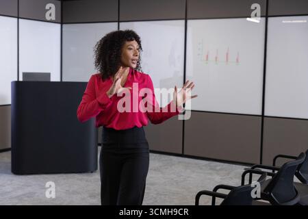 afroamerikanerin in Geschäftskleidung, die Charts auf Bildschirmen und Gesten auf dem Podium präsentiert Stockfoto
