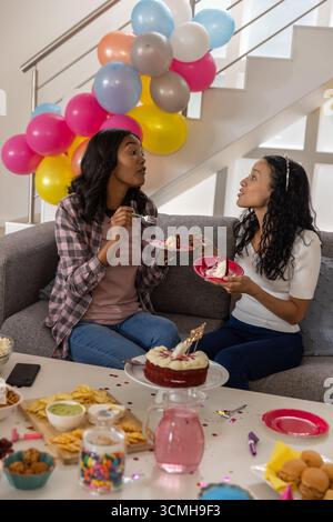 Die Mutter und die Tochter im Teenageralter halten Kuchenteller mit Gabeln, die zu Hause auf dem Sofa sitzen Stockfoto