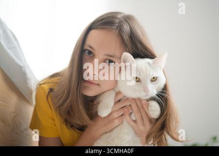 Eine heranwachsende Frau, die ihre unberührte weiße Katze in liebevoller Umarmung hält. Schöne Demonstration von Tierfreundschaft und Hingabe. Stockfoto