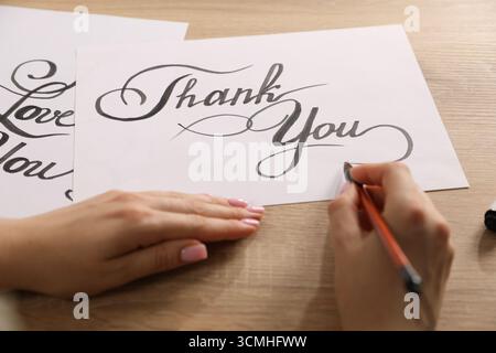 Kalligraphie. Frau mit Pinsel schreibt Worte Danke auf Blatt Papier am Holztisch, Nahaufnahme Stockfoto