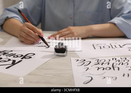 Kalligraphie. Frau mit Pinselschrift auf Blatt Papier am Holztisch, Nahaufnahme Stockfoto