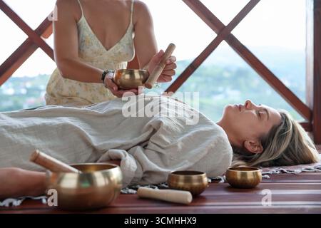 Frau, die sich einer Klangschüssel unterzieht und drinnen auf dem Boden liegt Stockfoto