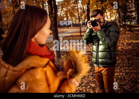 Paare genießen einen romantischen Herbsttag und fangen Momente mit einer Kamera in einem Park, umgeben von lebhaftem Herbstlaub, ein Stockfoto