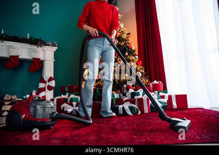 Junge Frau saugt in einem festlichen Haus, das für Weihnachten mit Geschenken, einem Baum und gemütlichen Winterferien dekoriert ist. Stockfoto