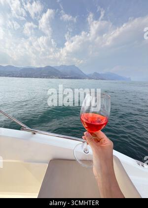 Ein Glas Aperol Cocktail aus nächster Nähe aus der ersten Person vor der Kulisse des Gardasees bei einer Motorbootfahrt Stockfoto