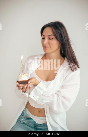 Eine junge Frau, die Kerze auf ihrem Geburtstagskuchen ausbläst. Geburtstagsfeier Stockfoto