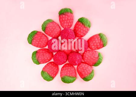 Gummiartige Erdbeerbonbons und runde Bonbons in Blumenform mit einem herzförmigen Bonbon in der Mitte auf rosa Hintergrund Stockfoto