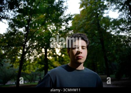 Porträt eines jungen Mannes, der in einem Park steht und das Sonnenlicht durch die Bäume filtert Stockfoto