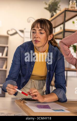 Verschiedene Kollegen lehnen sich im Büro über den Schreibtisch und untersuchen gedruckte Karten mit Haftnotizen Stockfoto