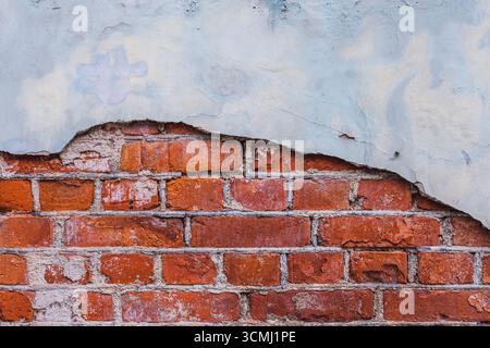 Nahaufnahme einer alten, verwitterten Ziegelwand mit erheblichen Teilen der weißen Putzbeschichtung, die sich abblättert und die roten Ziegelsteine freilegt Stockfoto