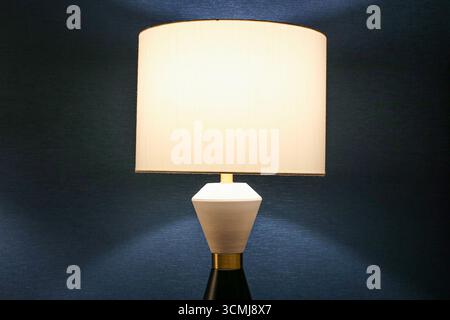 Die Nachtlampe leuchtet in einem dunklen Zimmer. Inneneinrichtung mit sanftem, warmem Licht. Eleganter Lampenschirm für Schlaf- oder Wohnbereich. Stockfoto
