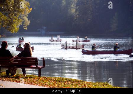 Eine ruhige Lagunenszene mit Kanus und Kajaks an einem nebeligen Morgen, umgeben von grünen Bäumen und einer Parkbank im Vordergrund. Bowness Park. Calgary Stockfoto