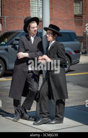 2 orthodoxe jüdische Jungen mit langem gelocktem Peyus unterhalten sich an einem milden Spätsommertag freundlich und lebhaft. Stockfoto